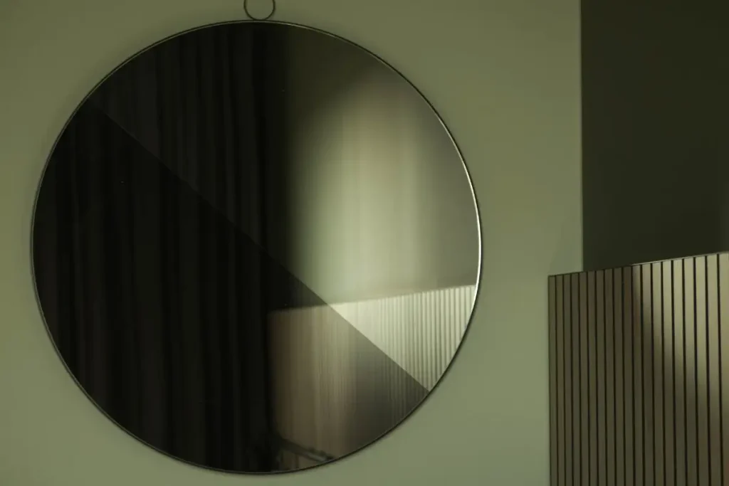 A minimalist round mirror reflecting a subtle play of light and deep shadows on a clean bathroom wall, demonstrating balance in interior design.