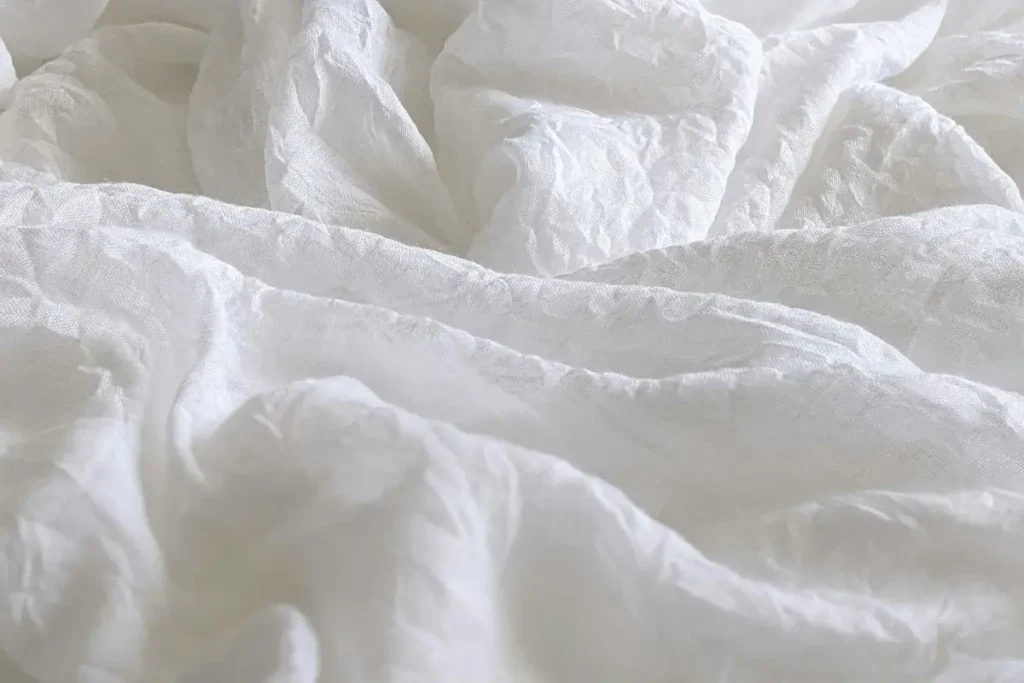 Close-up of natural linen bed sheets showing the breathable texture of the fabric.
