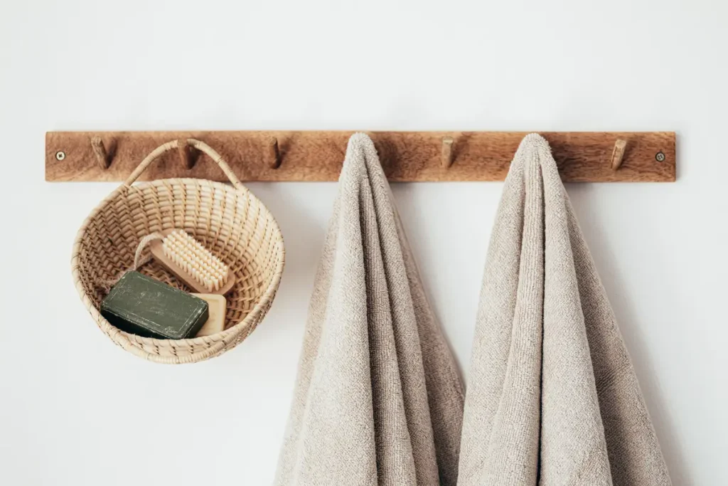Neutral beige towels and a small woven basket hanging on a wooden rack in a clean bathroom.